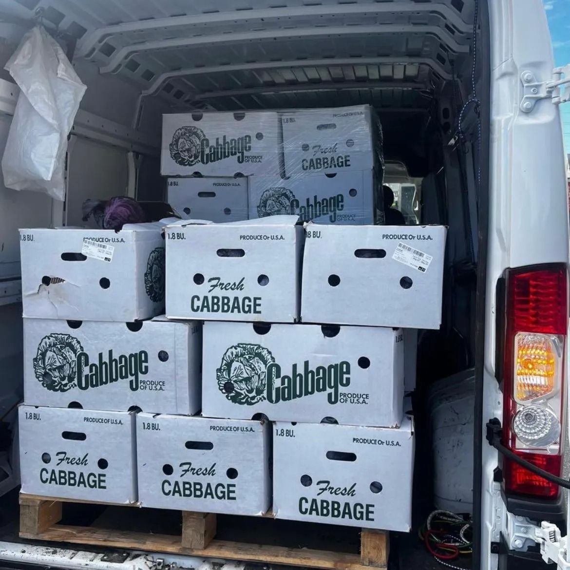 White van cargo area stacked with cardboard boxes labeled “Cabbage” and other produce logos