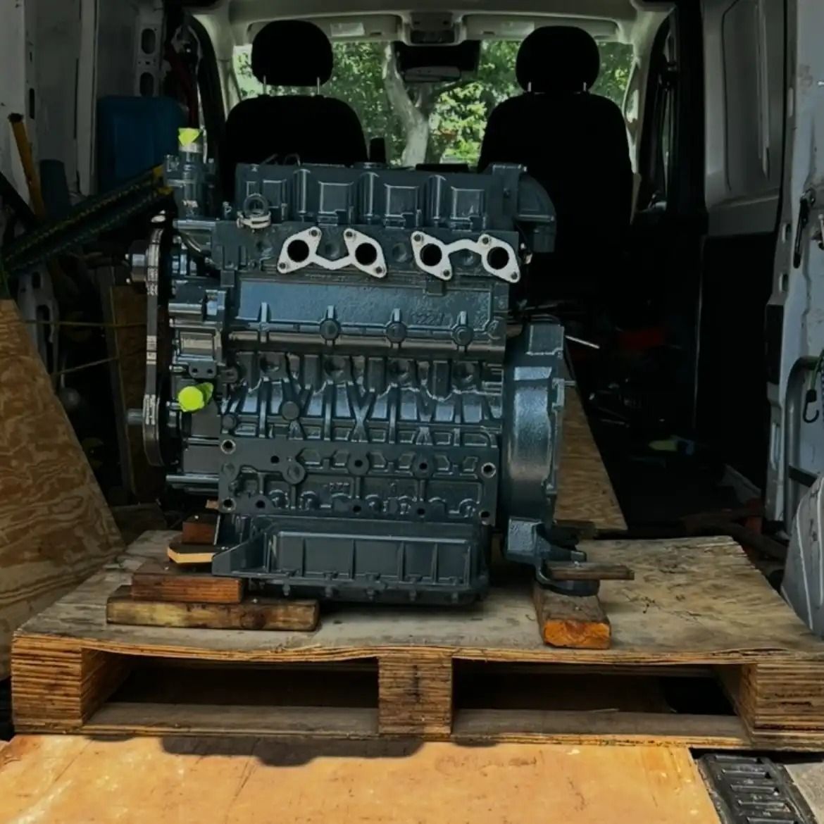 Engine block on a wooden pallet inside a van trunk.