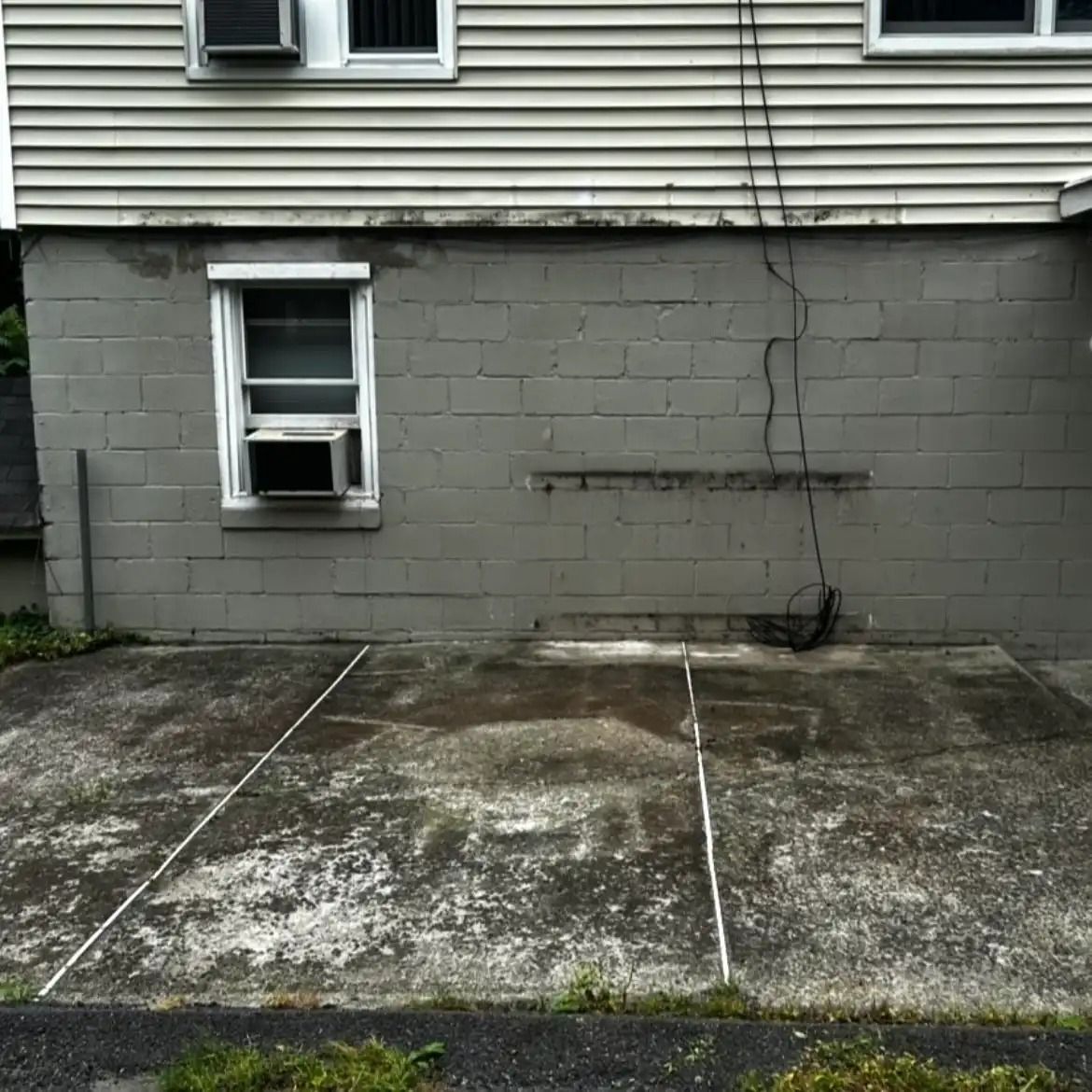 Cracked gray cinder block wall beside a small basement window and weathered concrete slab.