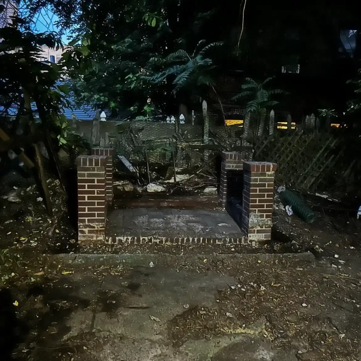 Brick-fronted garden bench in a dimly lit, overgrown yard at night.
