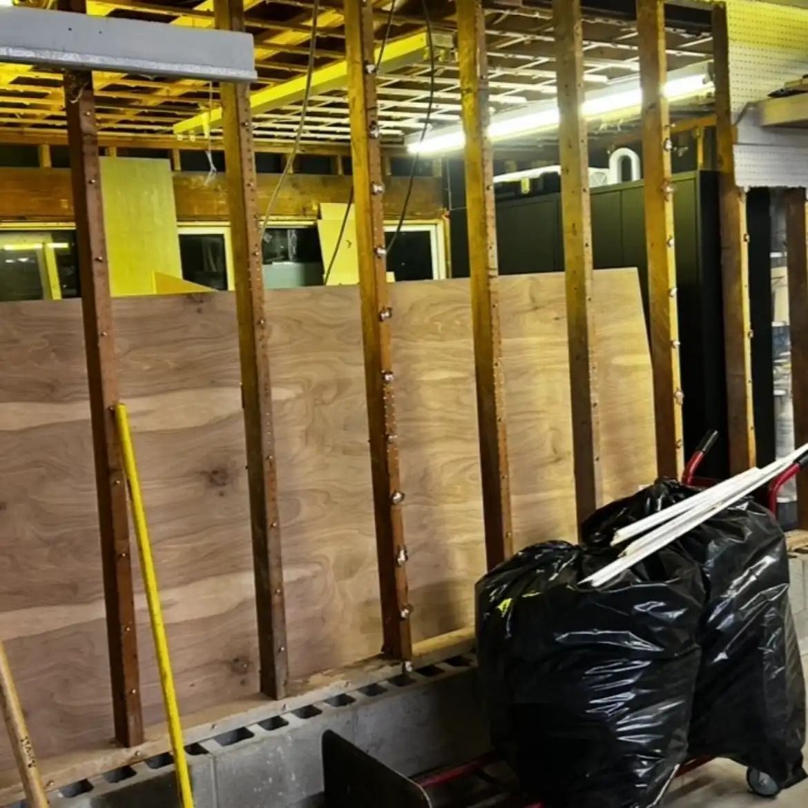 Construction area with plywood wall framing, exposed beams, and black trash bags in the foreground