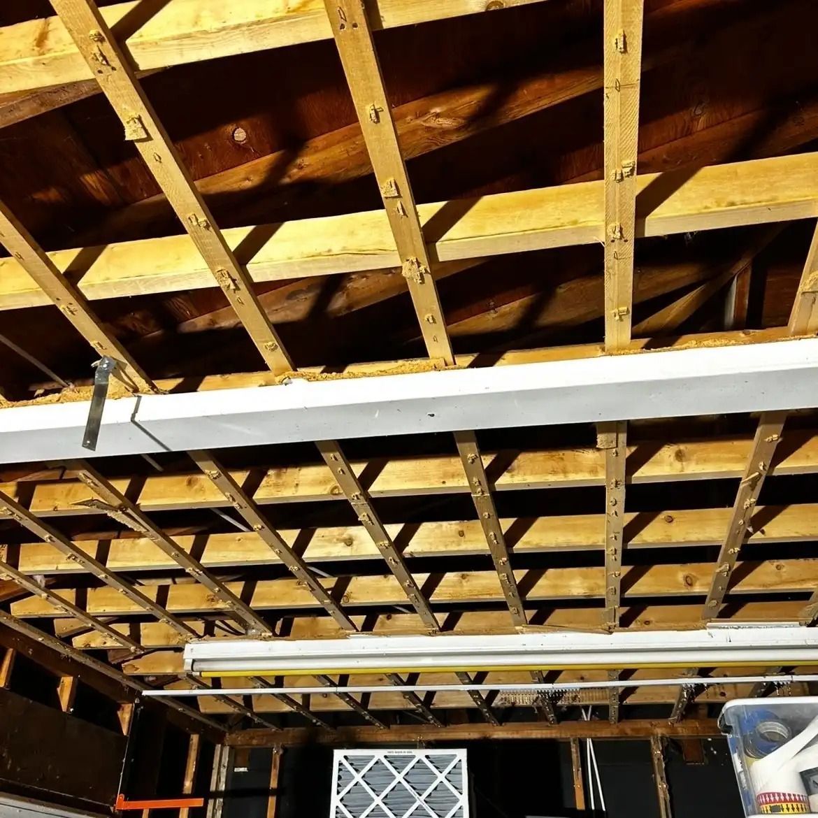 Exposed wooden garage ceiling with rafters and hanging fluorescent lights over a white-framed window.