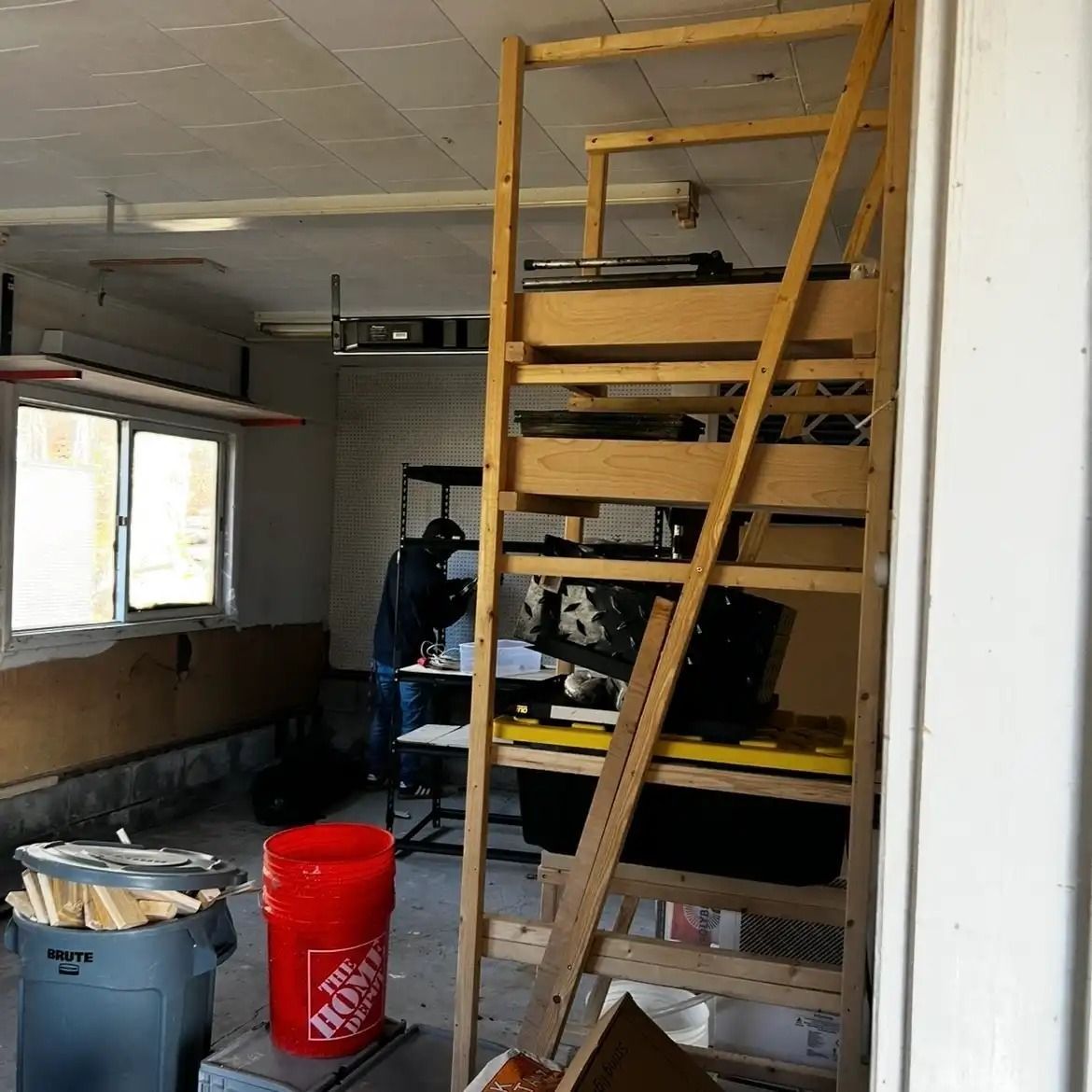 Interior room with wooden stairs, a red bucket, trash cans, and a window on the left