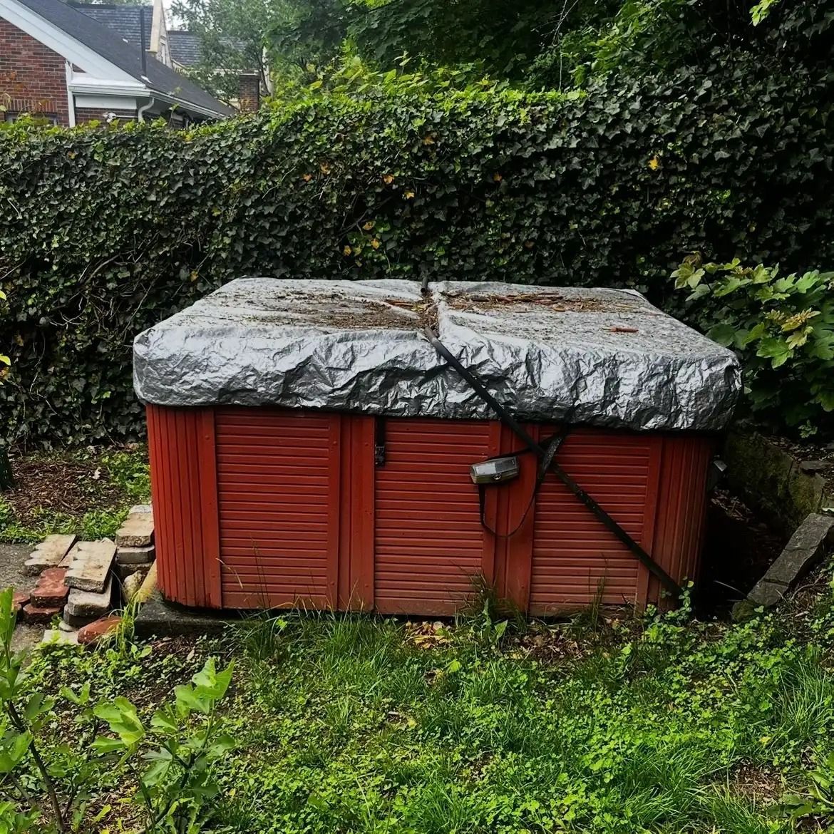 Red garden shed with a gray tarp roof, surrounded by grass and hedges.