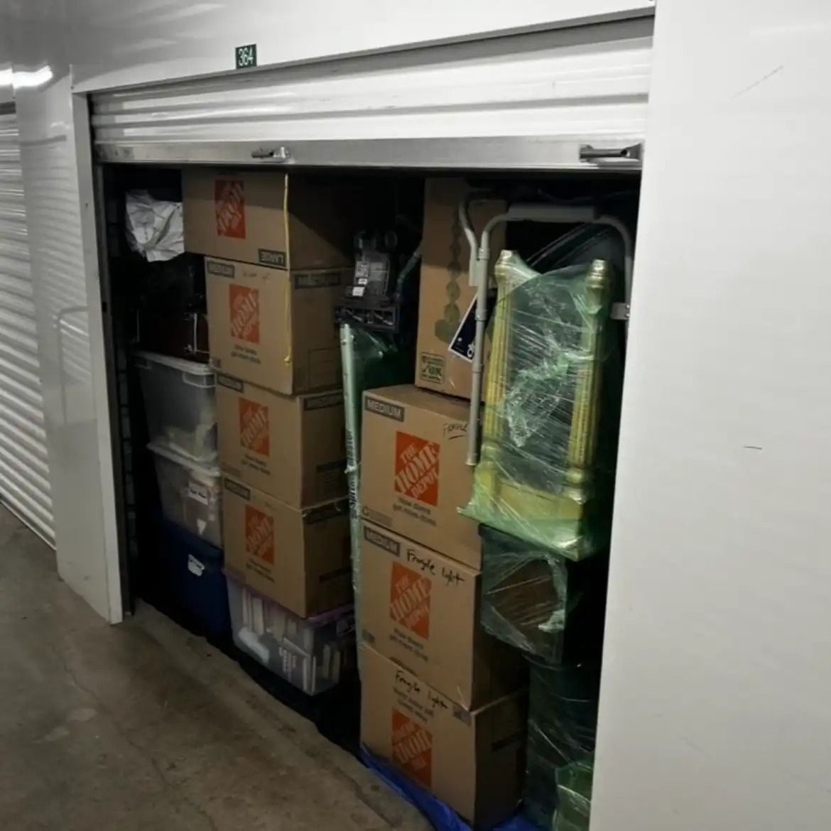Storage locker packed with stacked cardboard boxes and wrapped items behind a partially open roll-up door