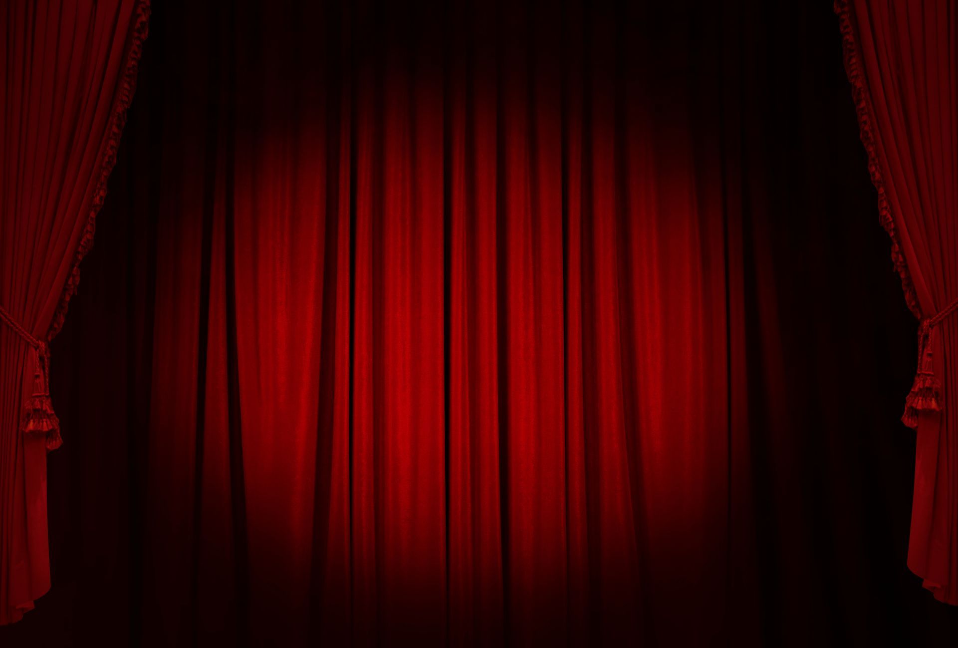 Red theater stage curtain with dark side drapes and a spotlight glow at center