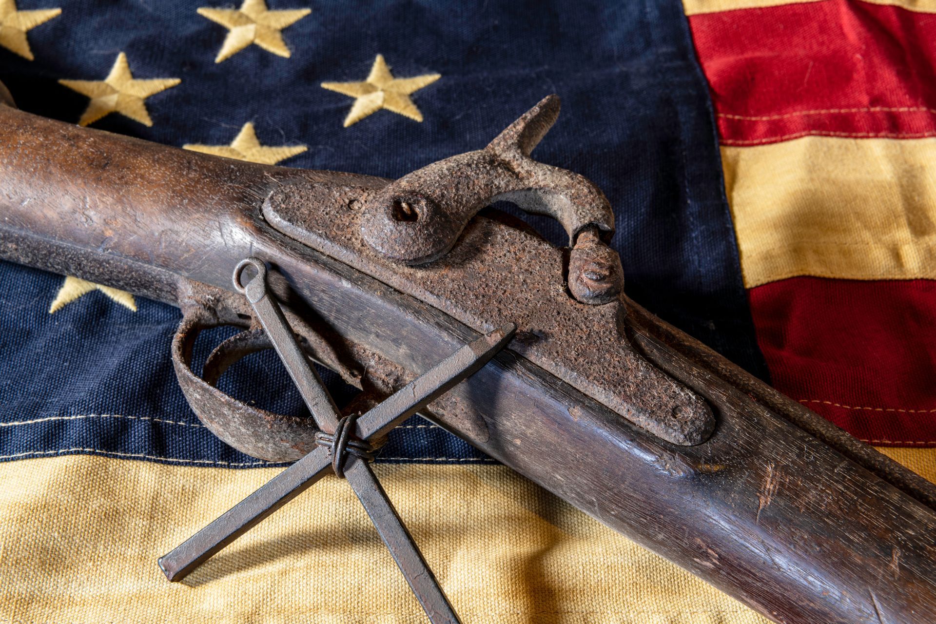 Rusty antique rifle on a U.S. flag backdrop with a folded bayonet attached
