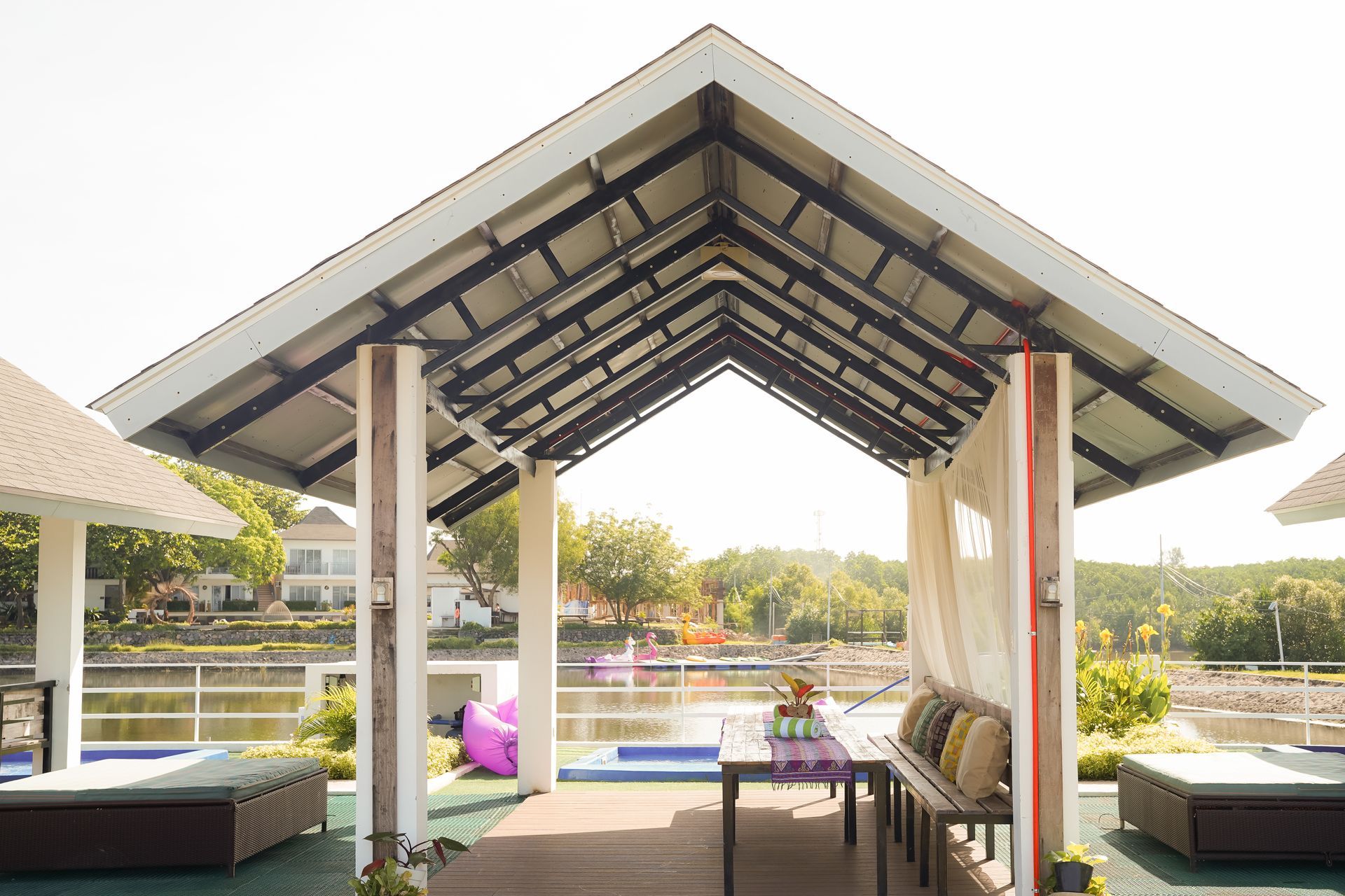 Gazebo over water with table set, cushions, and distant buildings.