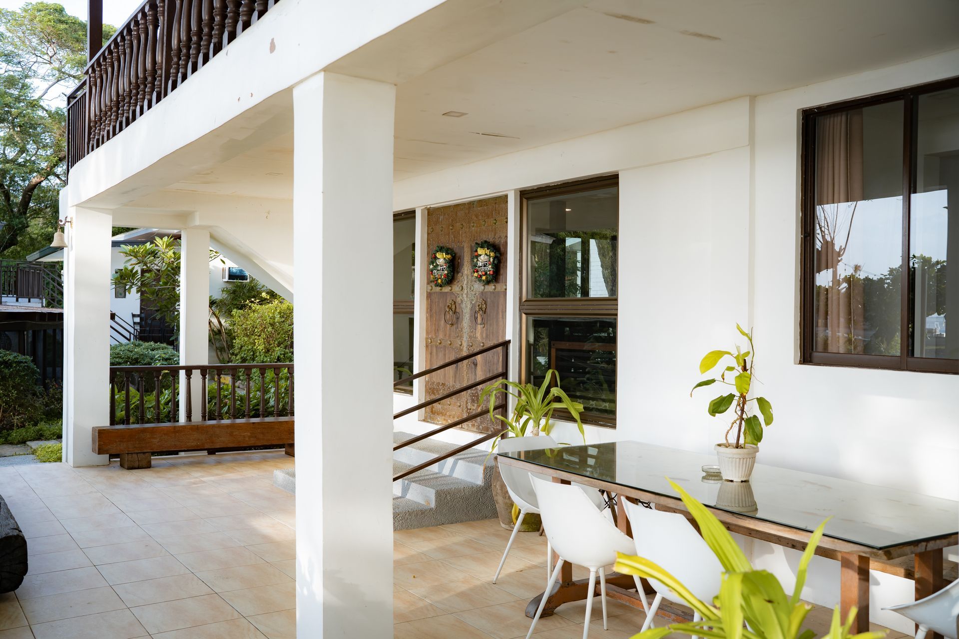 Outdoor patio with white columns, wooden railing, and glass table with white chairs.