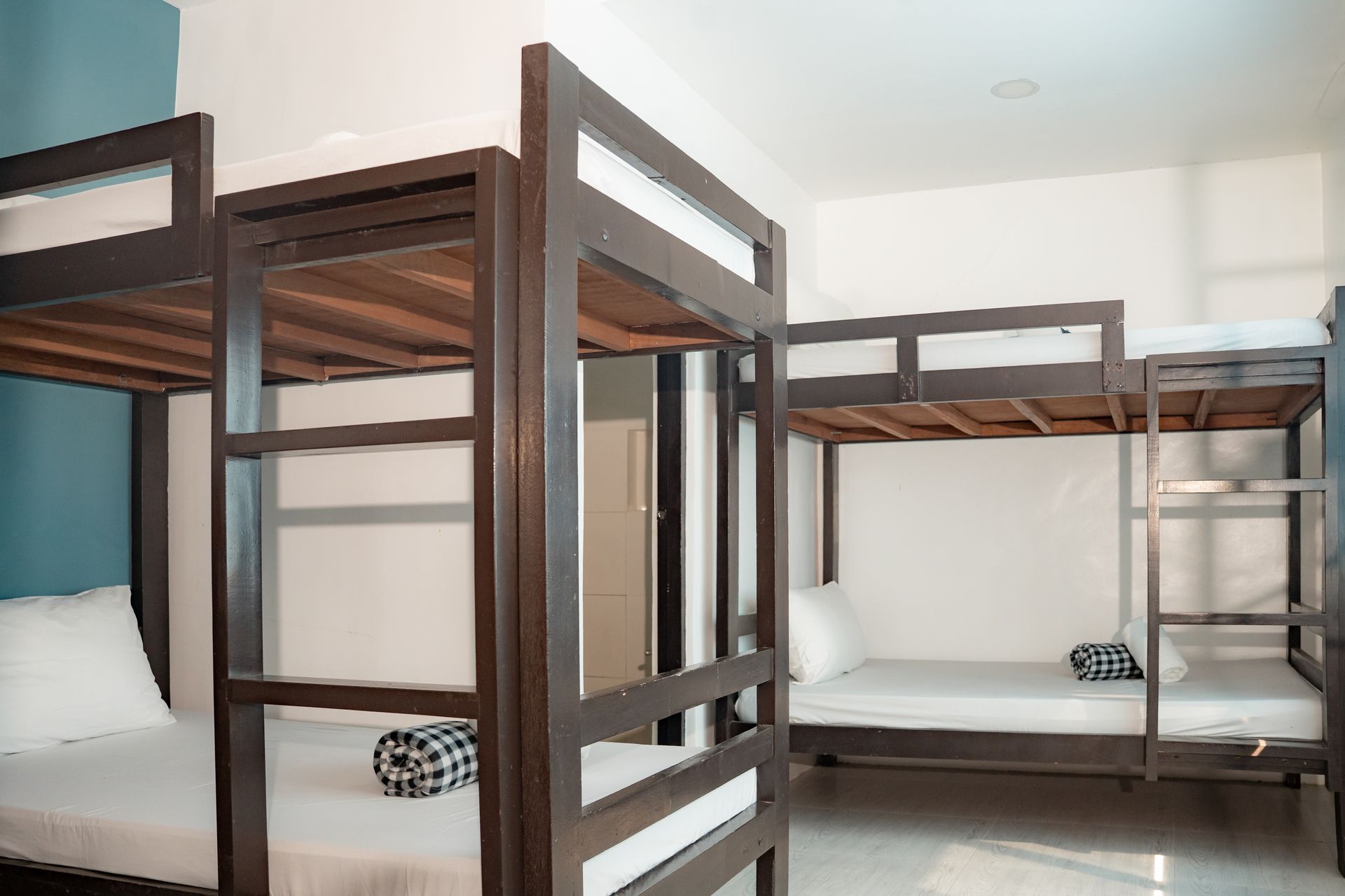 Bunk beds in a room. Brown wooden frames, white bedding, a rolled towel on each bed. White walls, light floor.