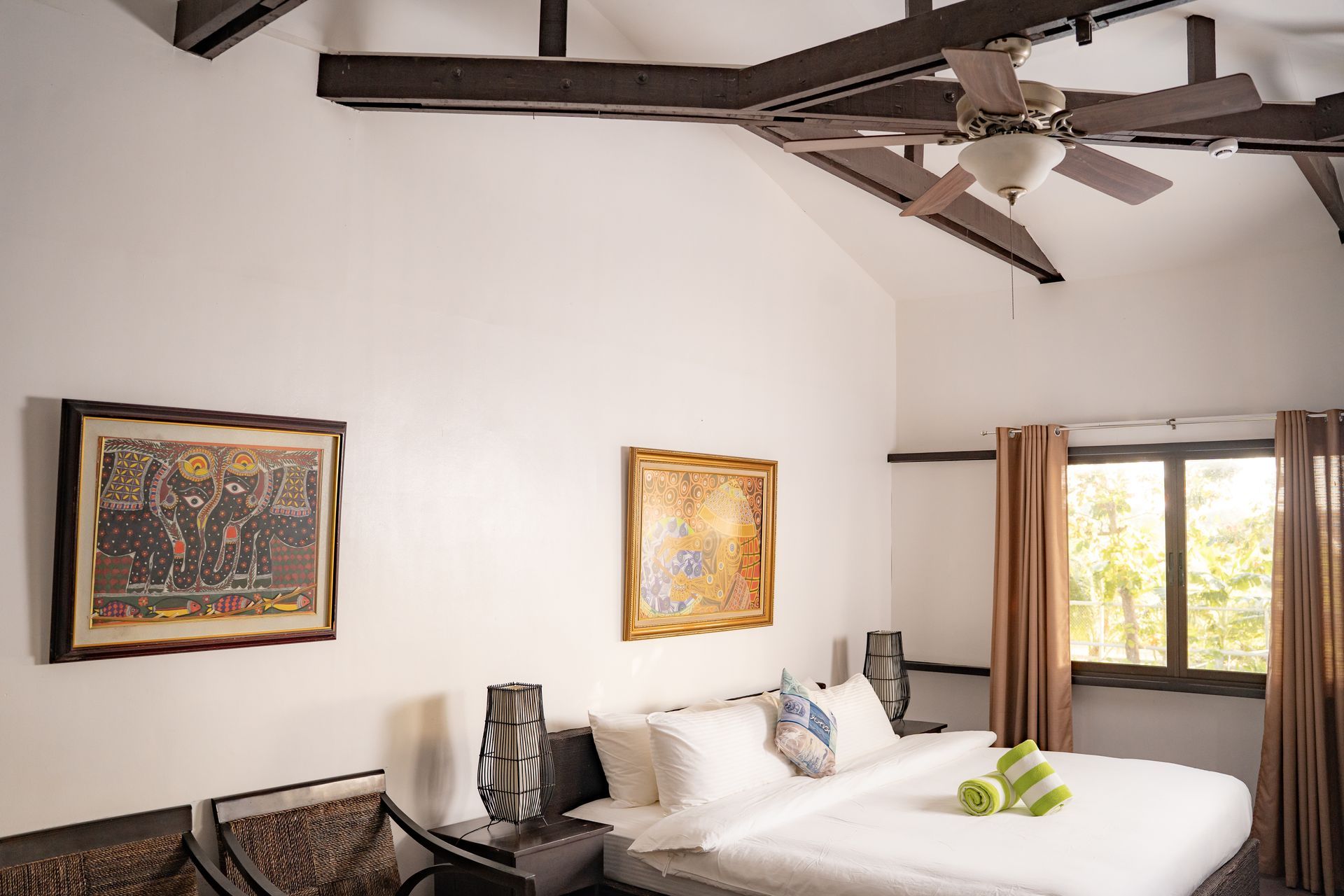 Bedroom with high ceiling, exposed beams, king-size bed, artwork, and window with curtains.