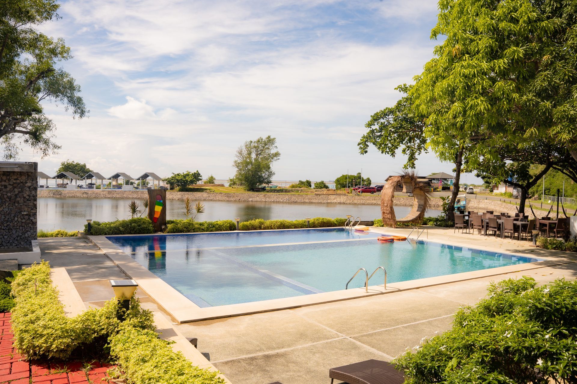 Swimming pool next to a body of water with trees and blue sky.