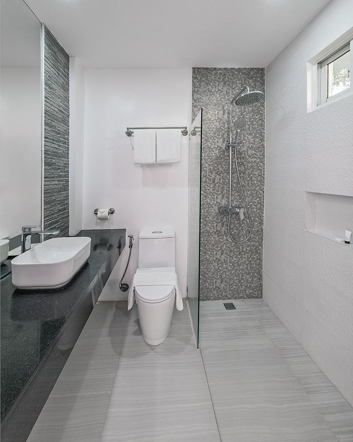Modern bathroom with white walls, gray stone shower, floating sink, and a toilet.
