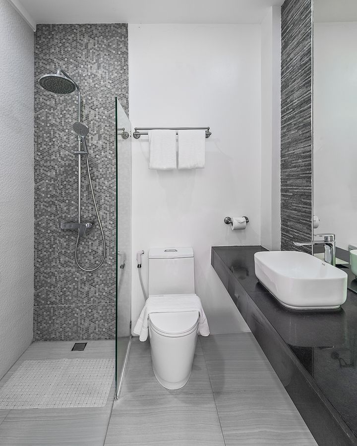 Modern bathroom with a shower, toilet, and sink. Features gray and white tile, and a long dark countertop.