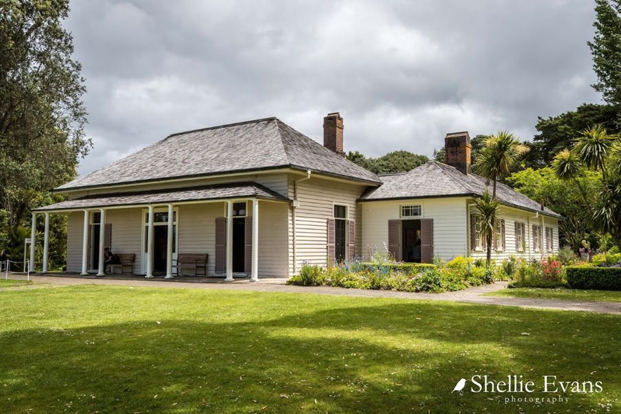 White country house with a covered porch, brick chimney, and large green lawn under cloudy skies