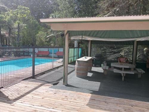 Covered poolside patio with table and benches beside a fenced swimming pool