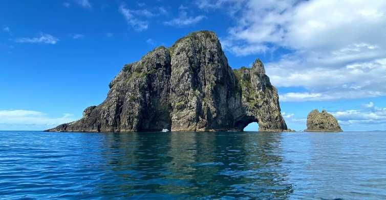 Rocky sea stack with a natural arch rising from bright blue ocean under a clear sky