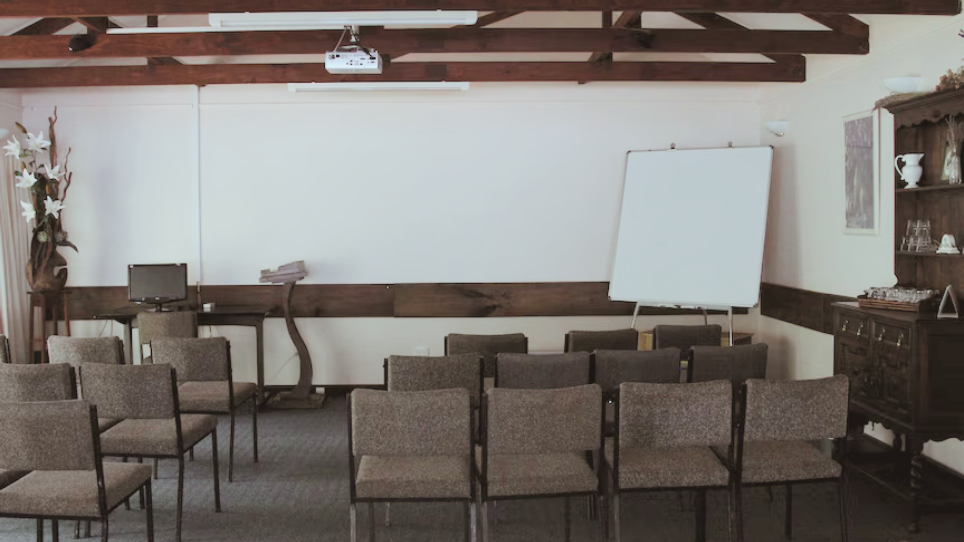Empty conference room with rows of chairs, a projection screen, and a flip chart on the front wall