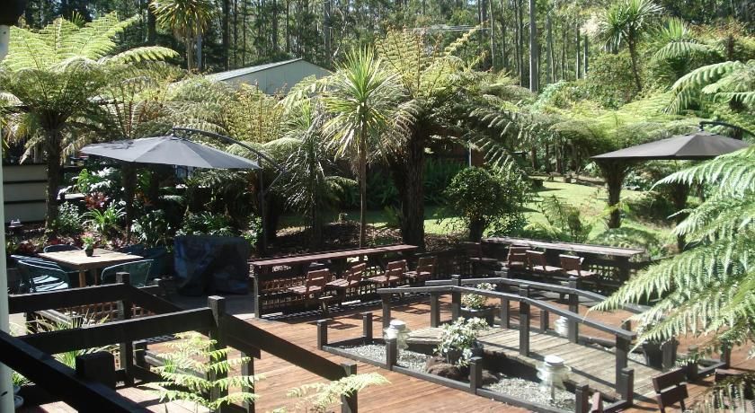 Outdoor café seating with wooden benches and black umbrellas in a lush green garden.