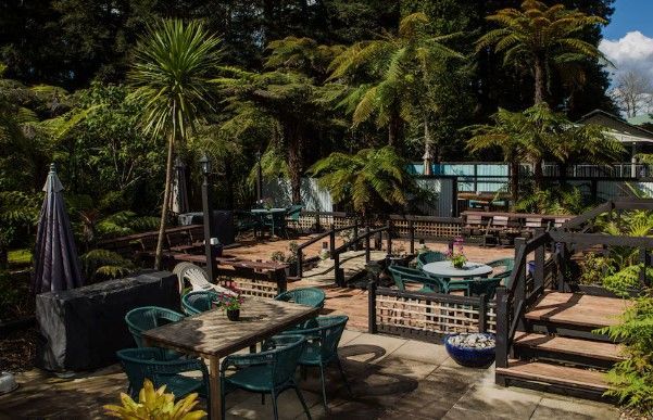 Outdoor patio with tables and chairs, surrounded by lush tropical plants and steps leading up to a terrace.
