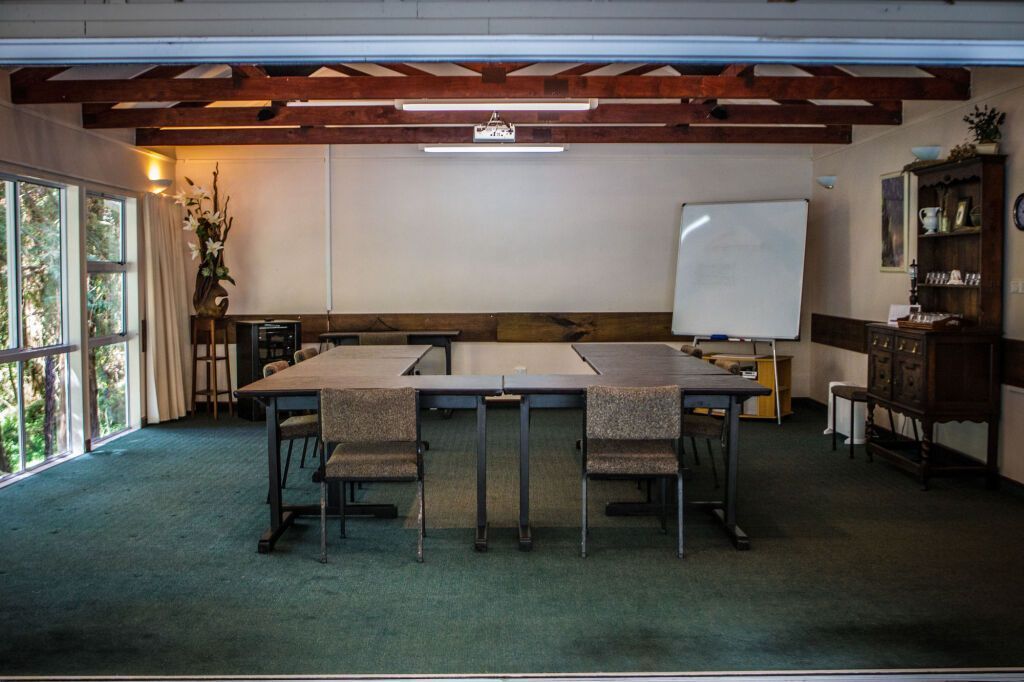 Conference room with long table, chairs, whiteboard, projector screen, and shelving under exposed wooden beams.