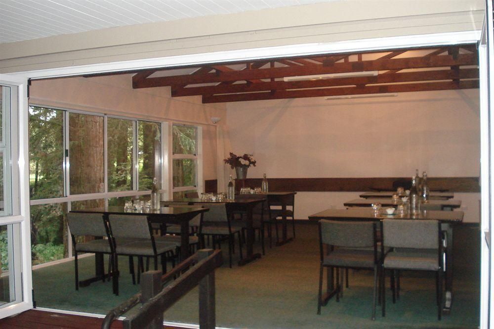 Indoor dining room with tables and chairs, large windows, and exposed wooden beams.
