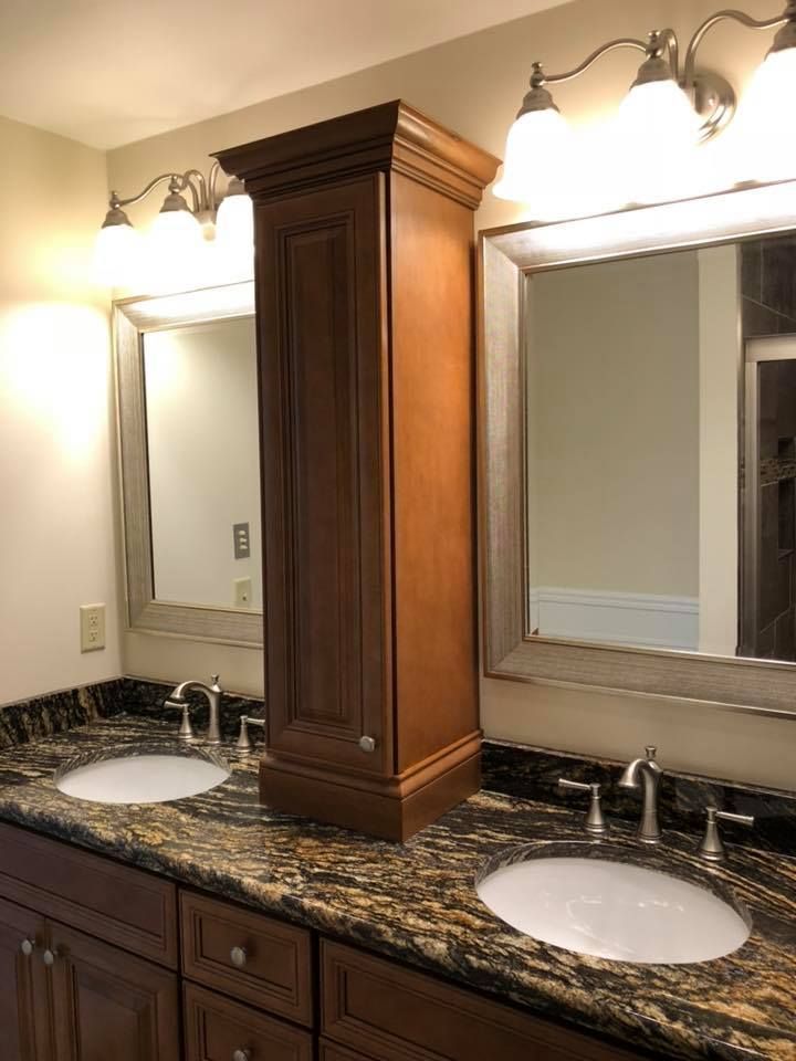 Bathroom with a dark wooden vanity, granite countertop, sinks, mirrors, and a tall central cabinet.