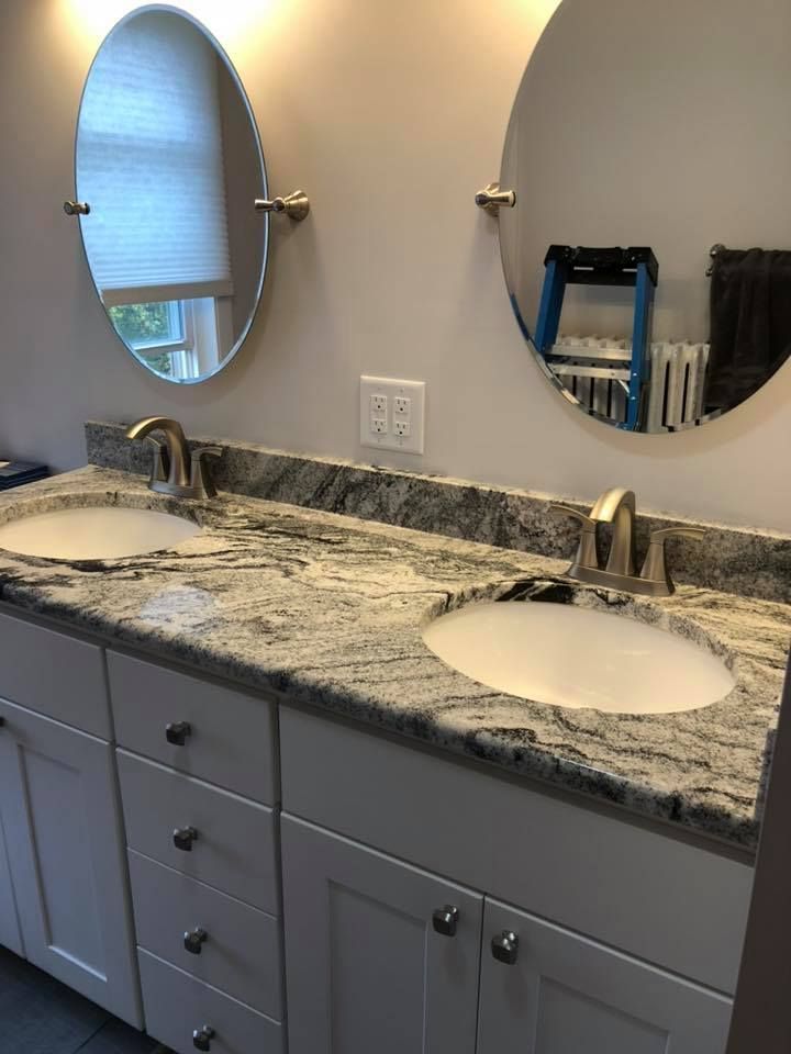 Bathroom with white vanity, granite countertop, two sinks, and oval mirrors.