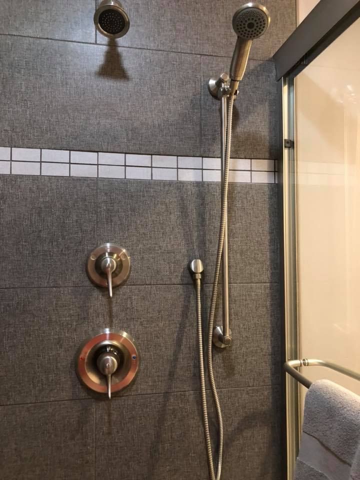 Shower with gray tile, silver fixtures, and glass door. Towel hangs on bar.