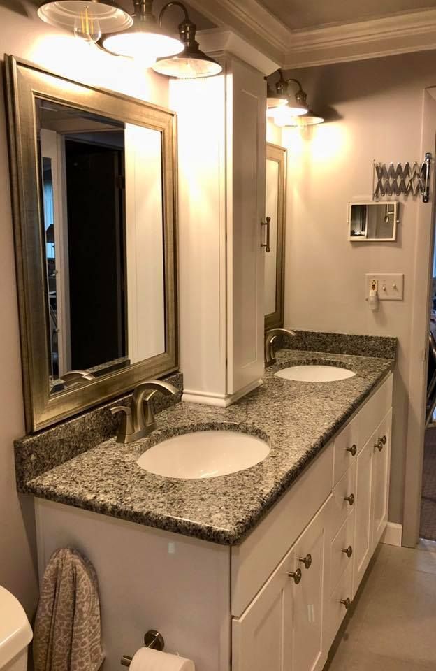 Bathroom with double sinks, white cabinets, granite countertop, mirror, and overhead lights.