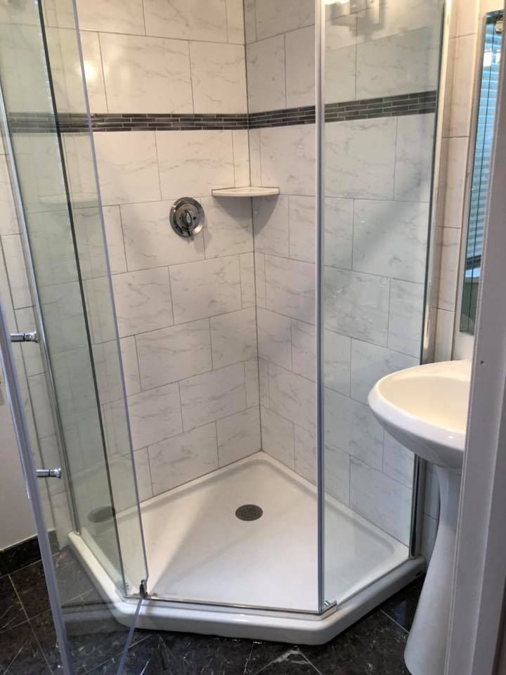 Corner shower with glass doors, white tiled walls, and a pedestal sink.