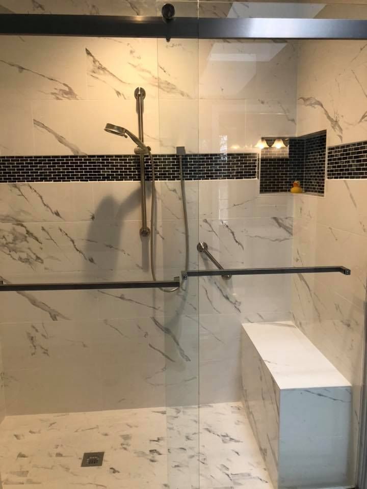 Modern tiled shower with glass door and built-in bench. Dark accents, black and white tile design.