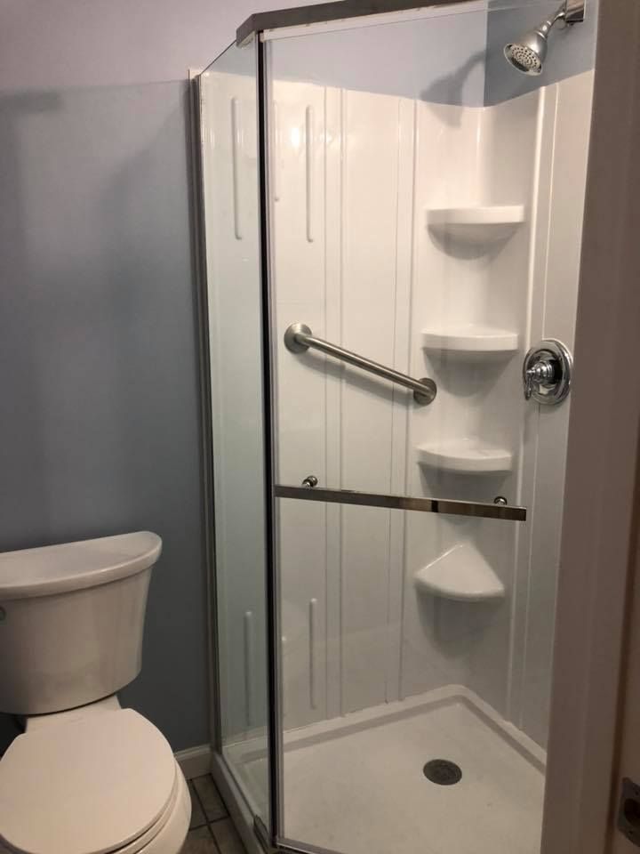 A corner shower with a glass door, grab bar, and built-in shelves next to a white toilet.