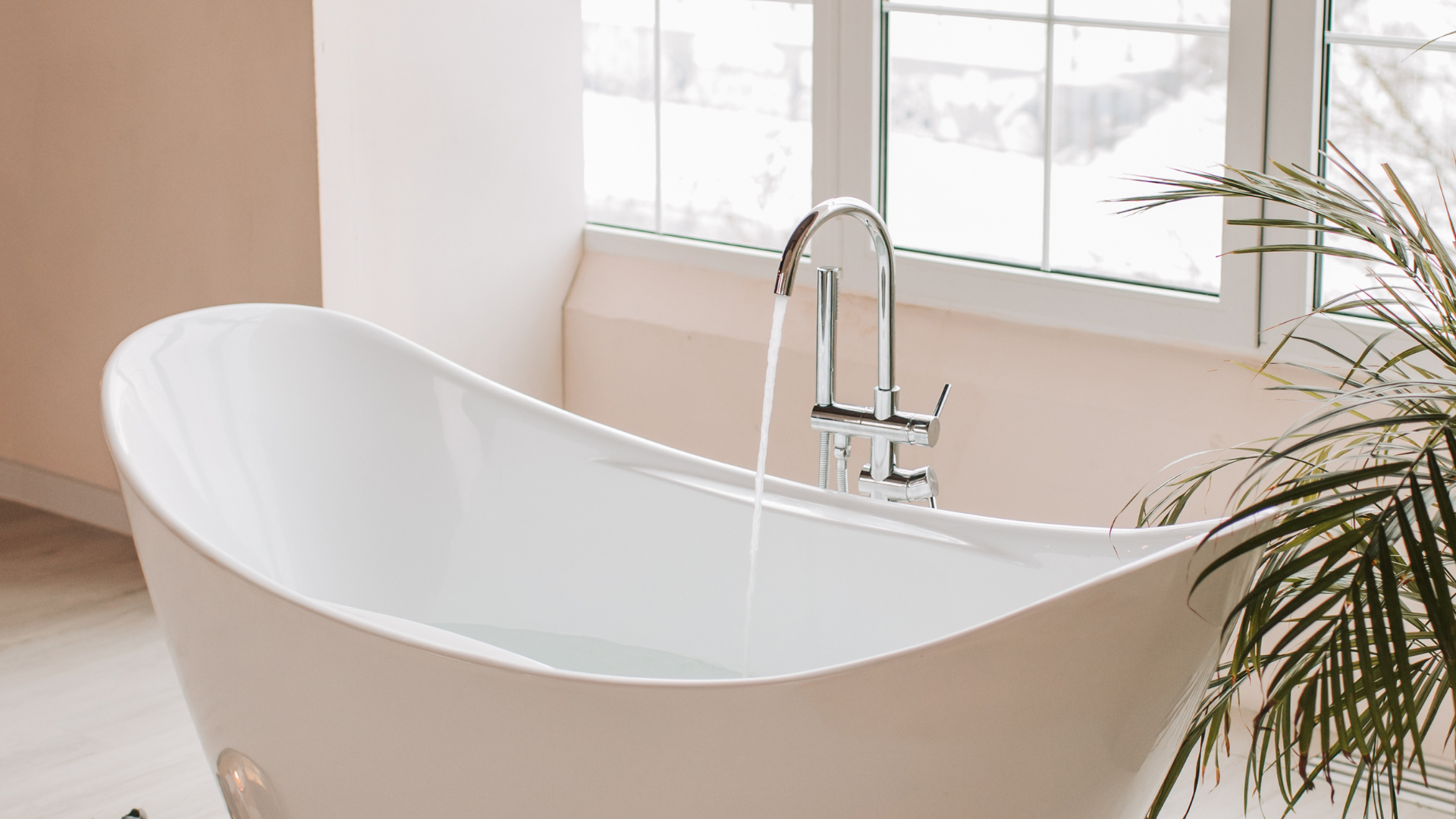 White freestanding bathtub with water running, near a window.
