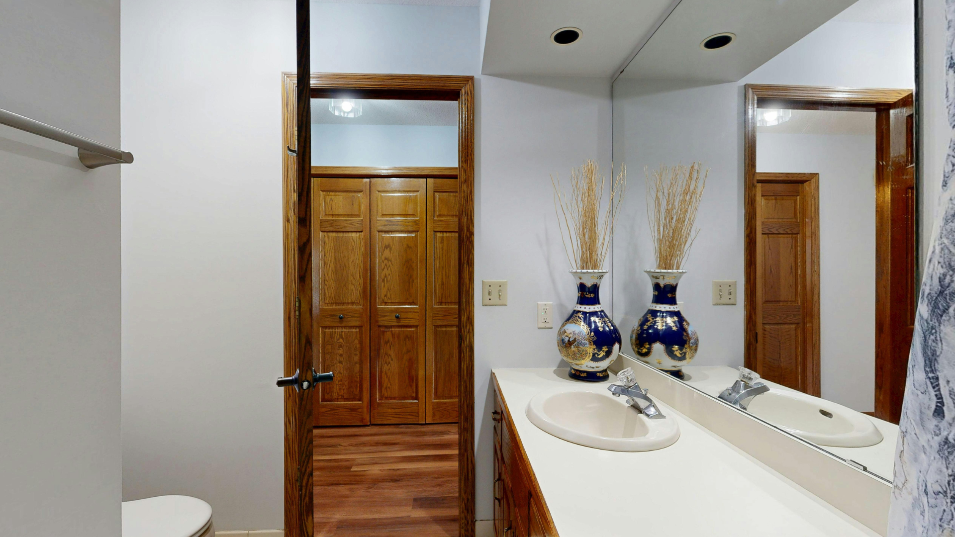 Bathroom with wood accents, a vanity with two vases, and a large mirror.