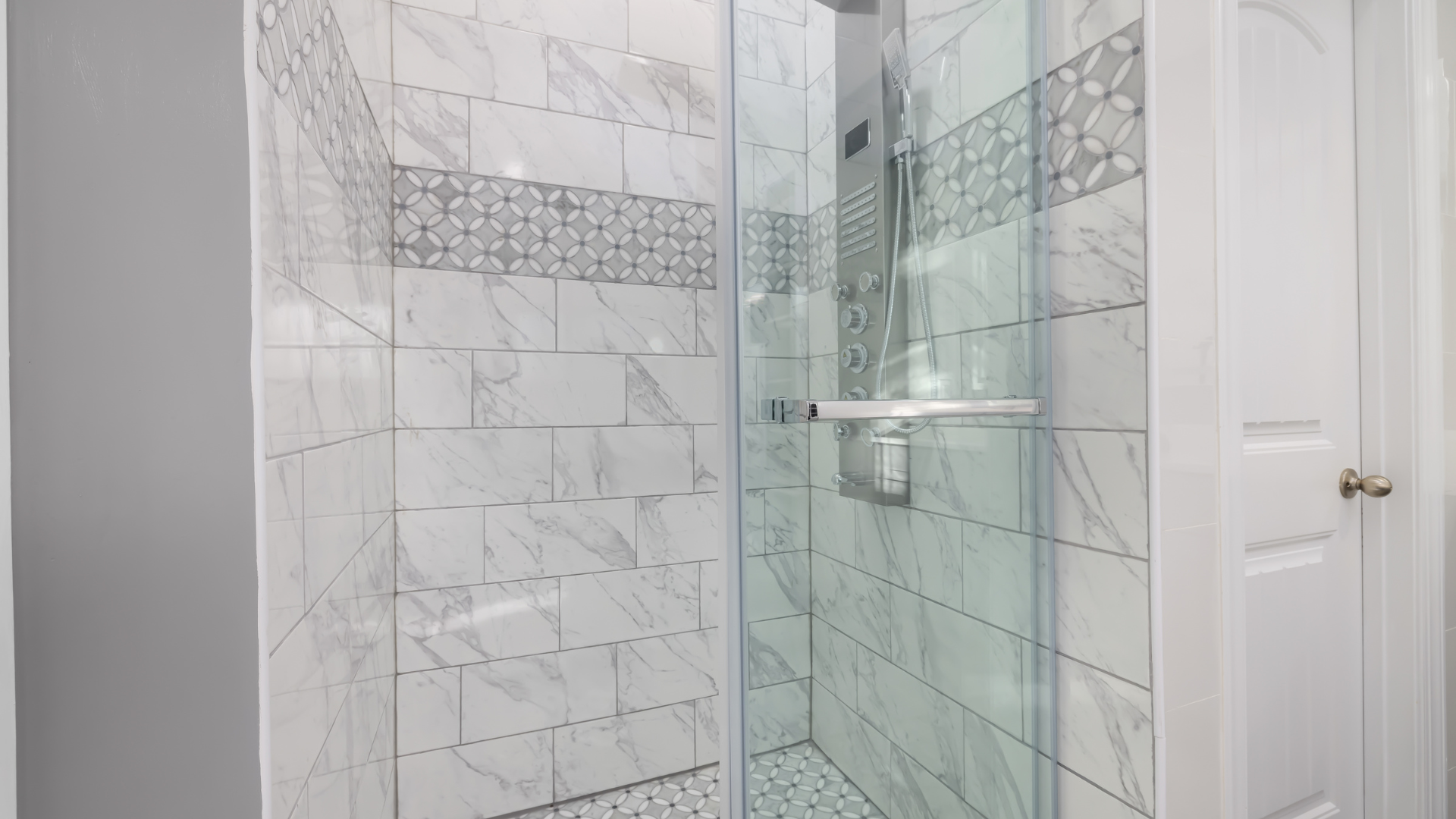 Glass shower with white marble-like tile and decorative accents. Silver shower fixtures are visible.