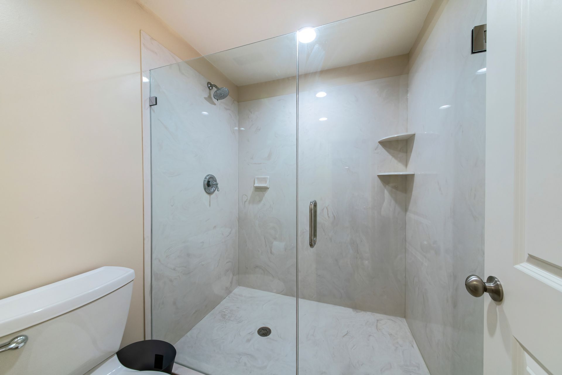 Modern bathroom with glass shower, toilet, and light-colored tile walls.
