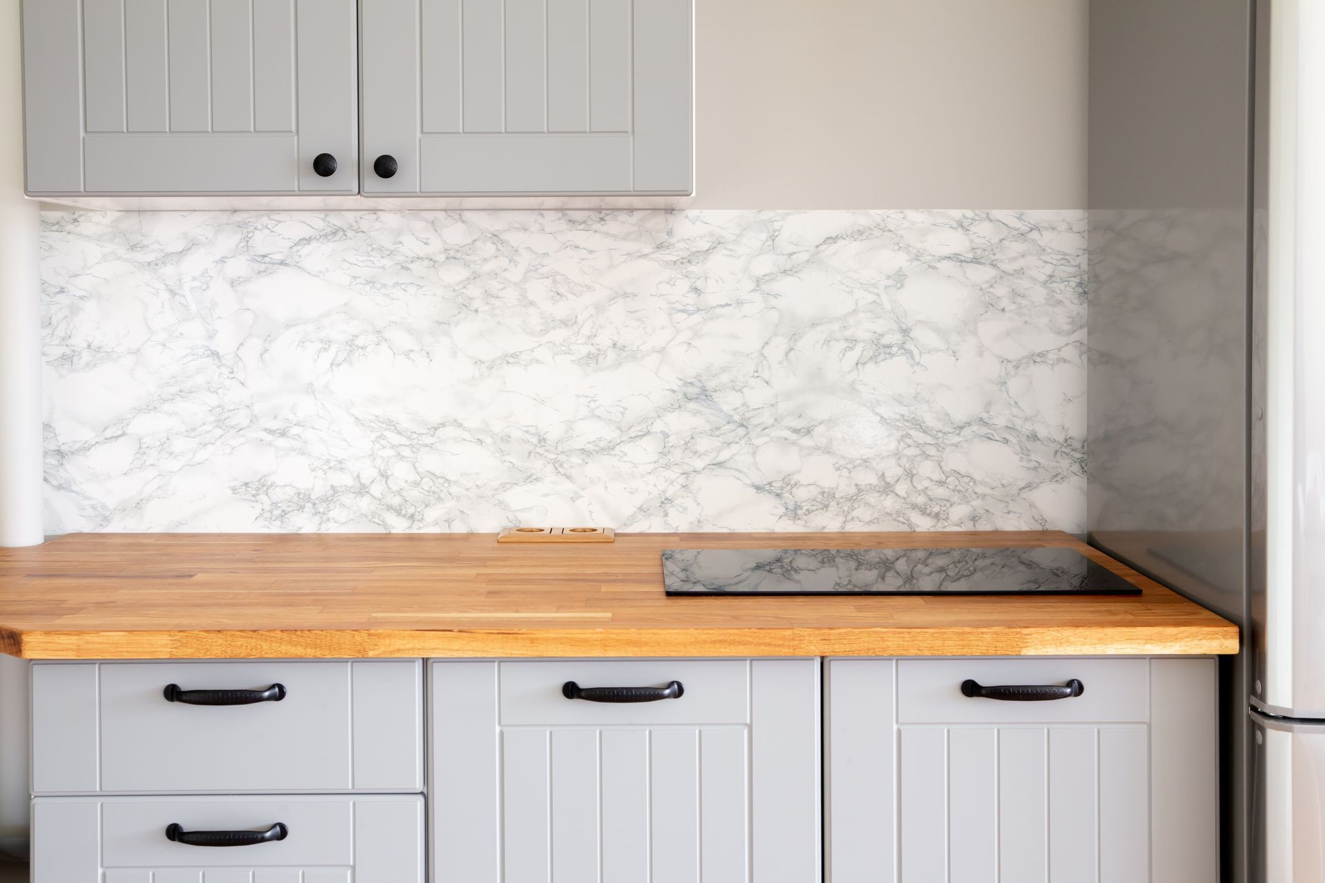 Gray kitchen with wooden countertop, marble backsplash, and cabinets.