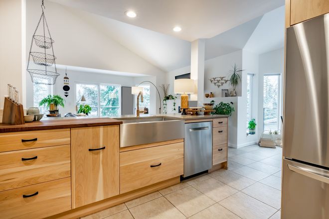 Bright, modern kitchen with light wood cabinets, stainless steel appliances, and large windows overlooking trees.