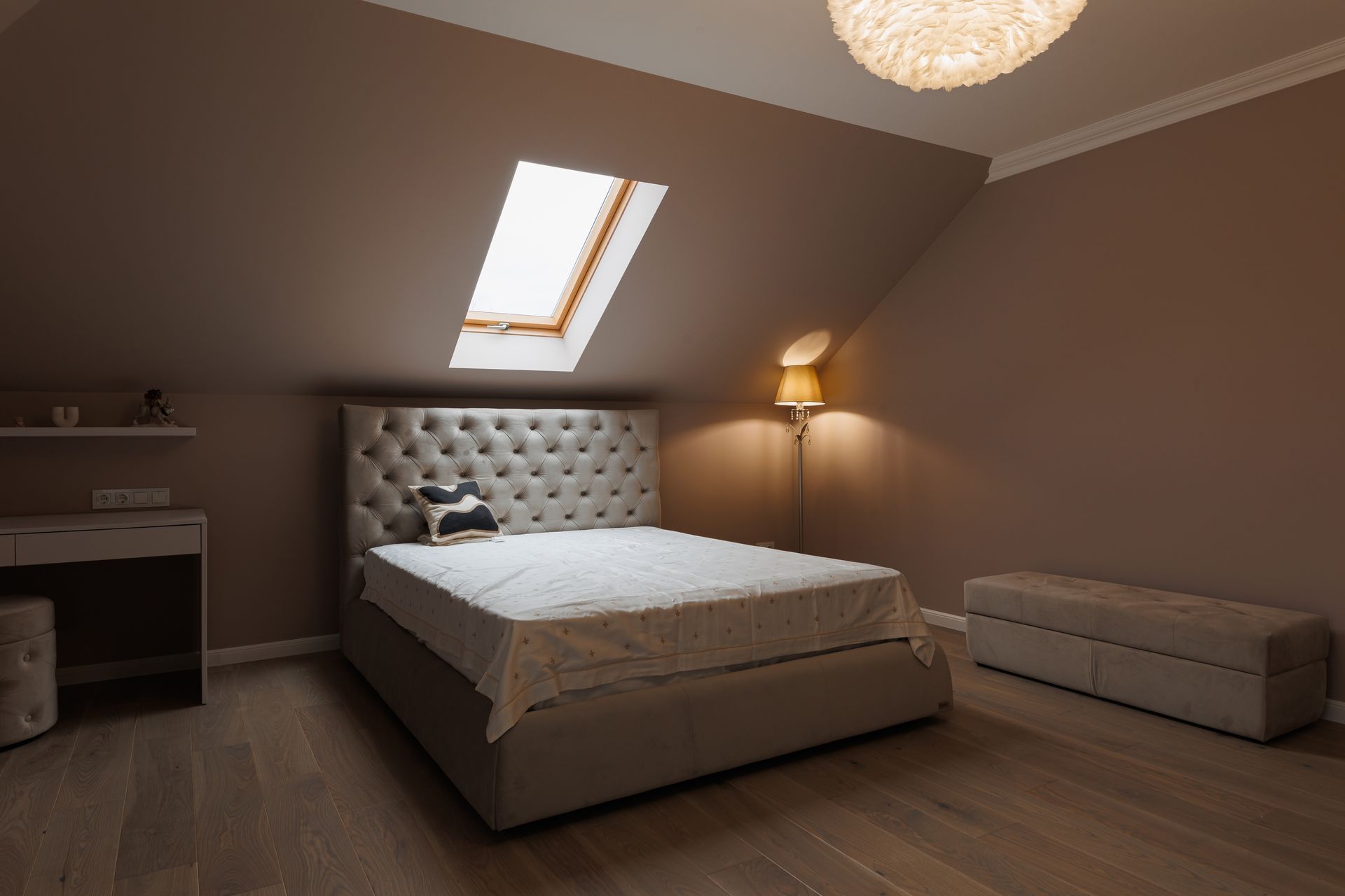 Bedroom with bed, desk, ottoman, skylight, and wall-mounted lamp.