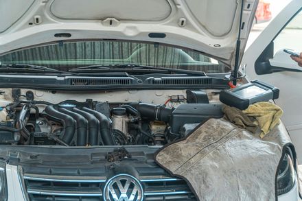 Open hood of a white Volkswagen car with engine components visible and a protective fender cover draped over the side.