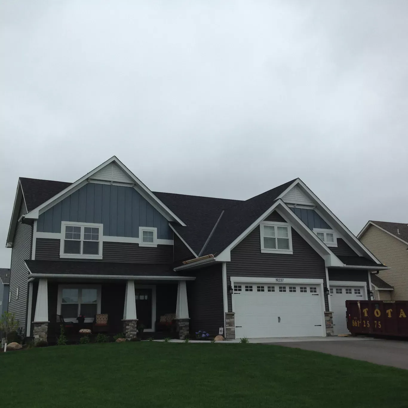 A modern house with a dark roof and blue siding against a gray sky. The garage door is white.