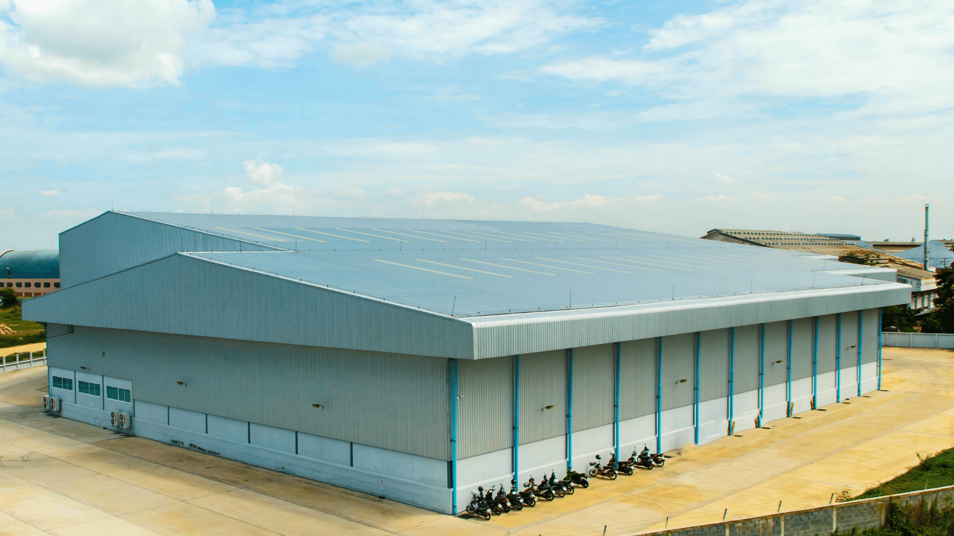 Large industrial warehouse with a light blue facade and a silver roof under a blue sky.