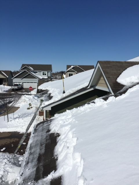 Snow-covered rooftops and yards in a residential area under a clear blue sky.