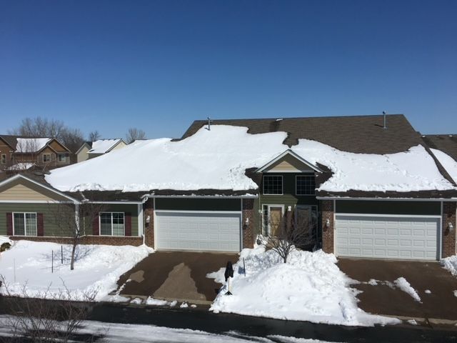 Townhouses with snow-covered roofs and driveways. The sky is clear blue.