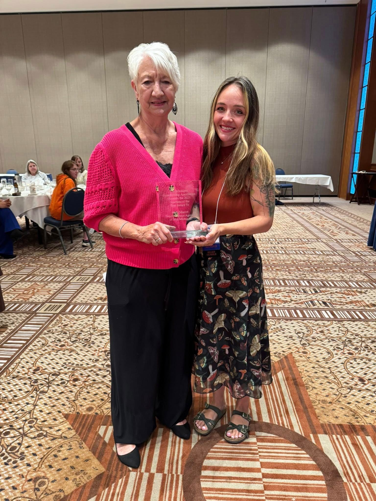 Two women smiling and holding a trophy in a banquet hall