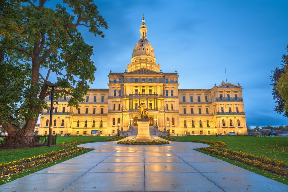 Illuminated historic government building at dusk with a central dome and grand steps, seen from a landscaped plaza