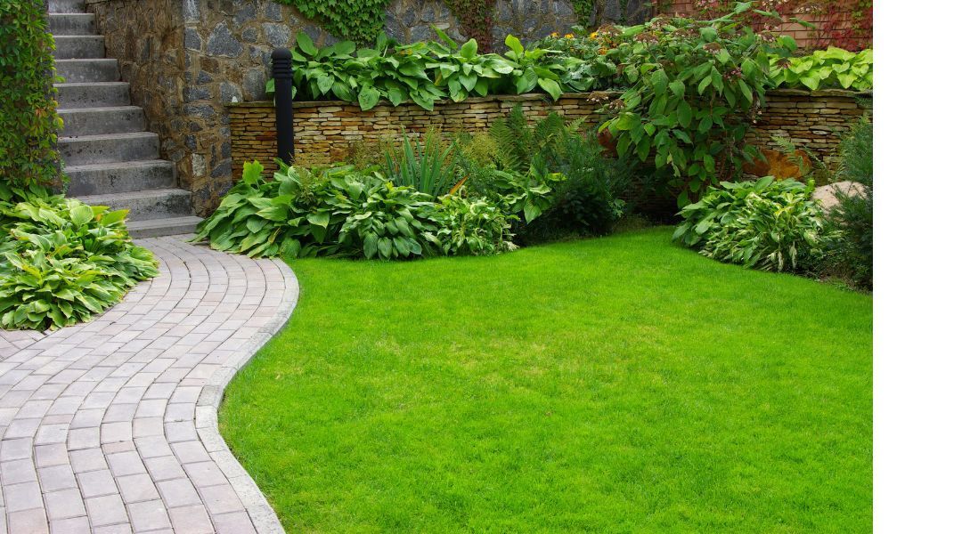 Curved stone path beside a bright green lawn and lush garden with stone steps in the background