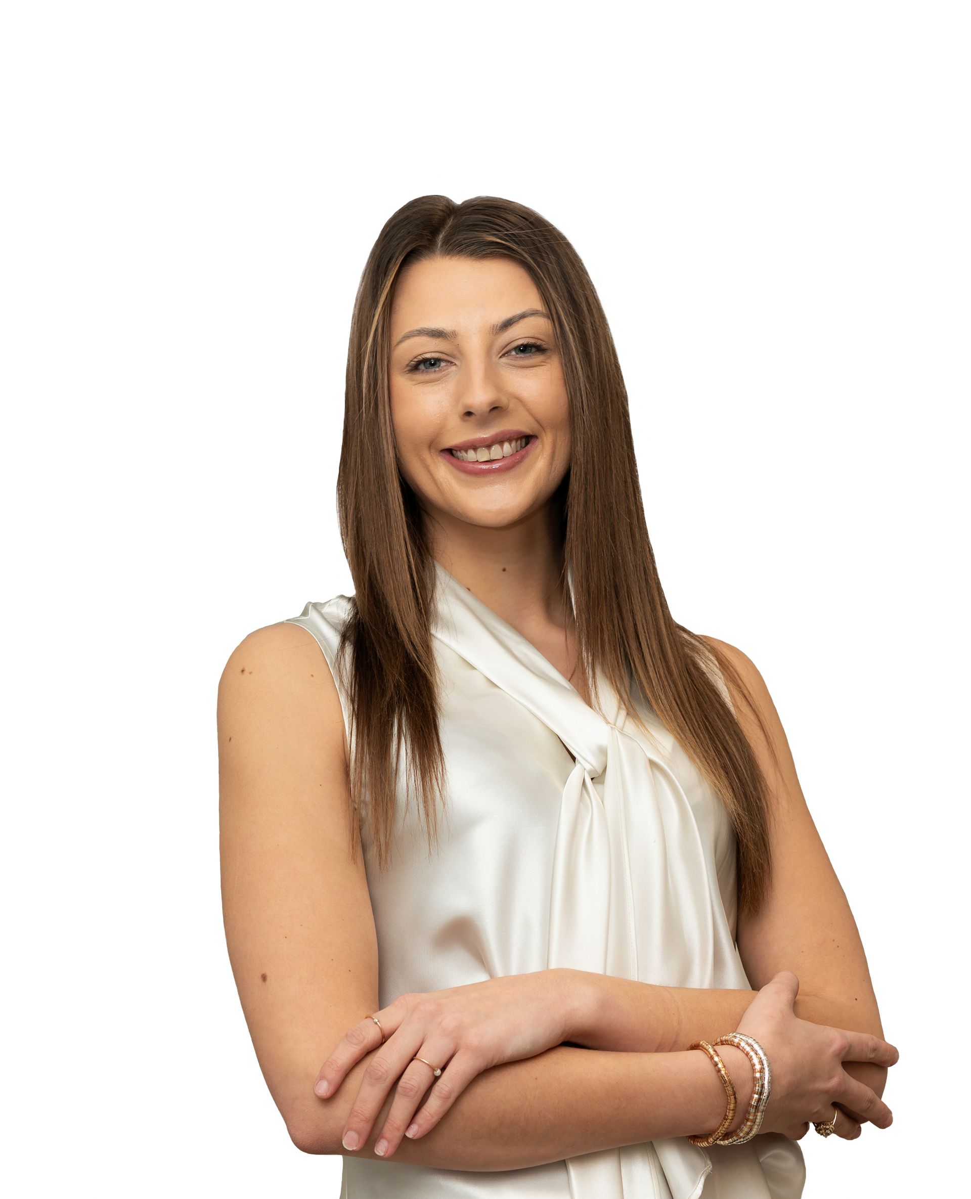 Smiling woman with long brown hair in a white blouse, standing with arms crossed on a white background