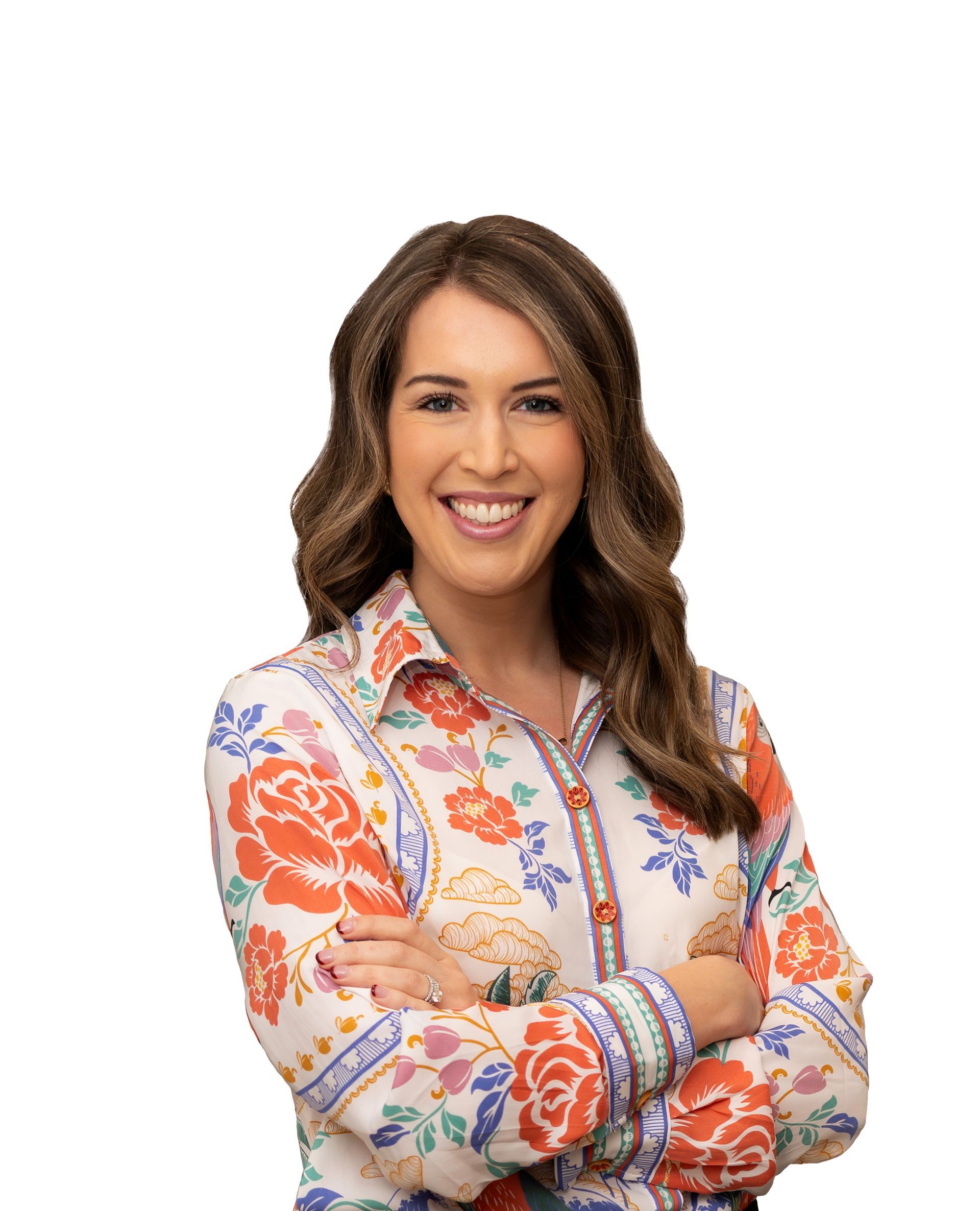 Smiling woman in a colorful floral blouse, standing with arms crossed on a white background